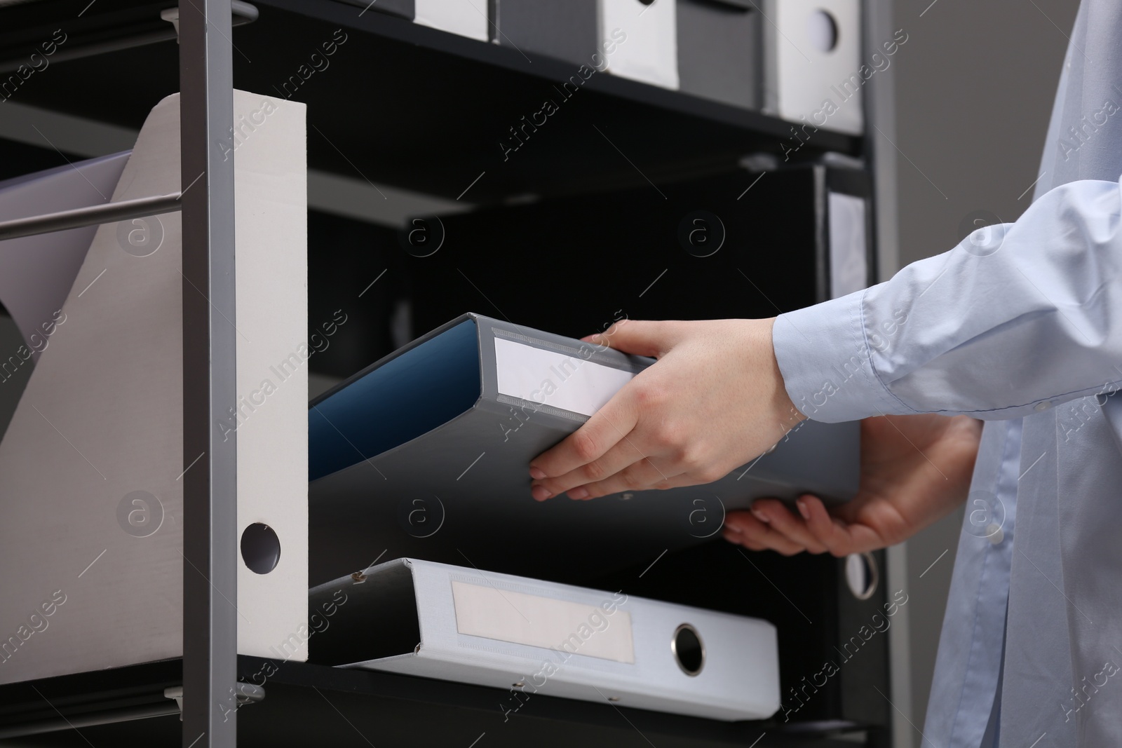 Photo of Woman taking folder with documents from shelf in office, closeup