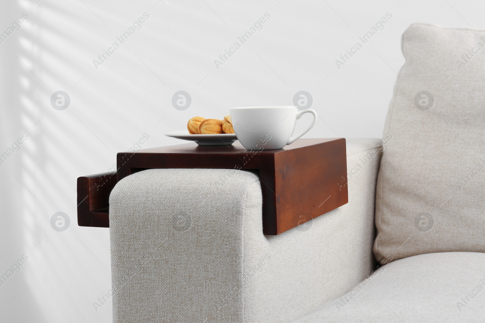 Photo of Cup of coffee and nut shaped cookies on sofa with wooden armrest table indoors. Interior element