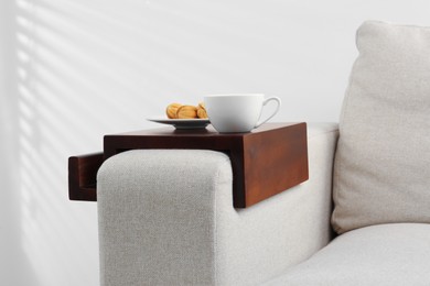 Photo of Cup of coffee and nut shaped cookies on sofa with wooden armrest table indoors. Interior element