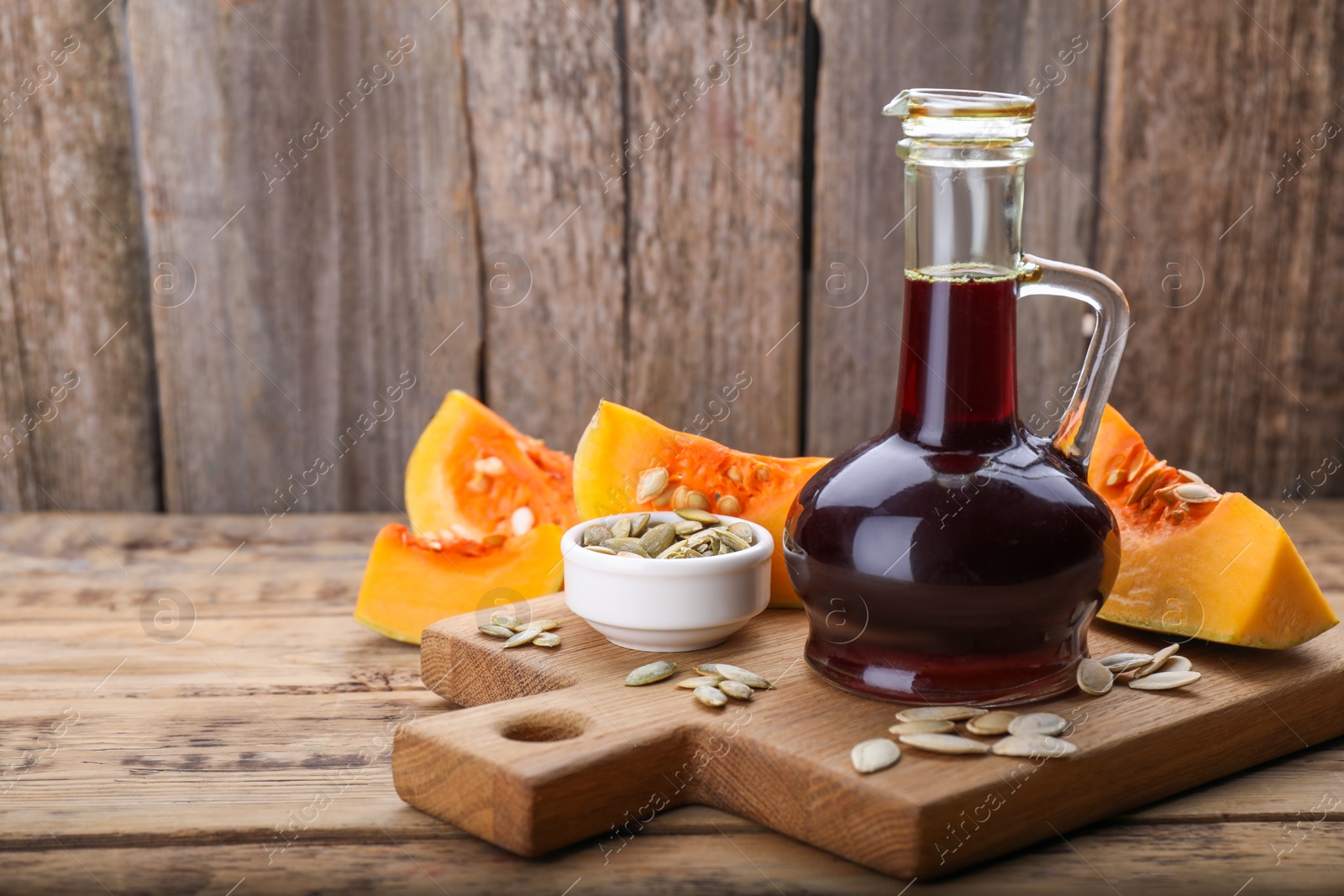 Photo of Fresh pumpkin seed oil in glass jug on wooden table. Space for text