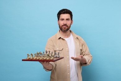 Handsome man holding chessboard with game pieces on light blue background