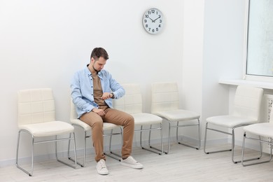 Photo of Man looking at wrist watch and waiting for appointment indoors