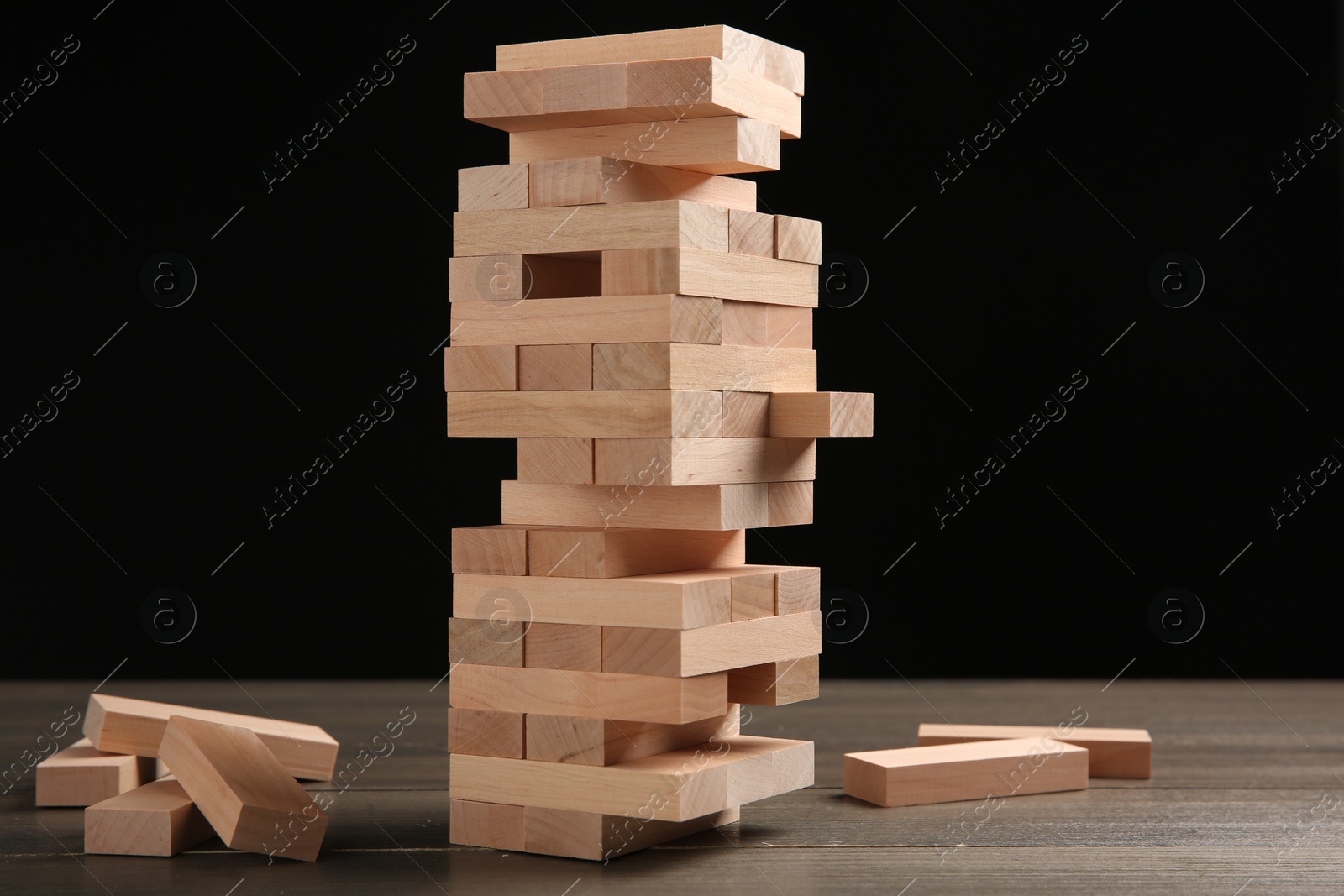 Photo of Jenga game. Tower made of wooden blocks on table against black background