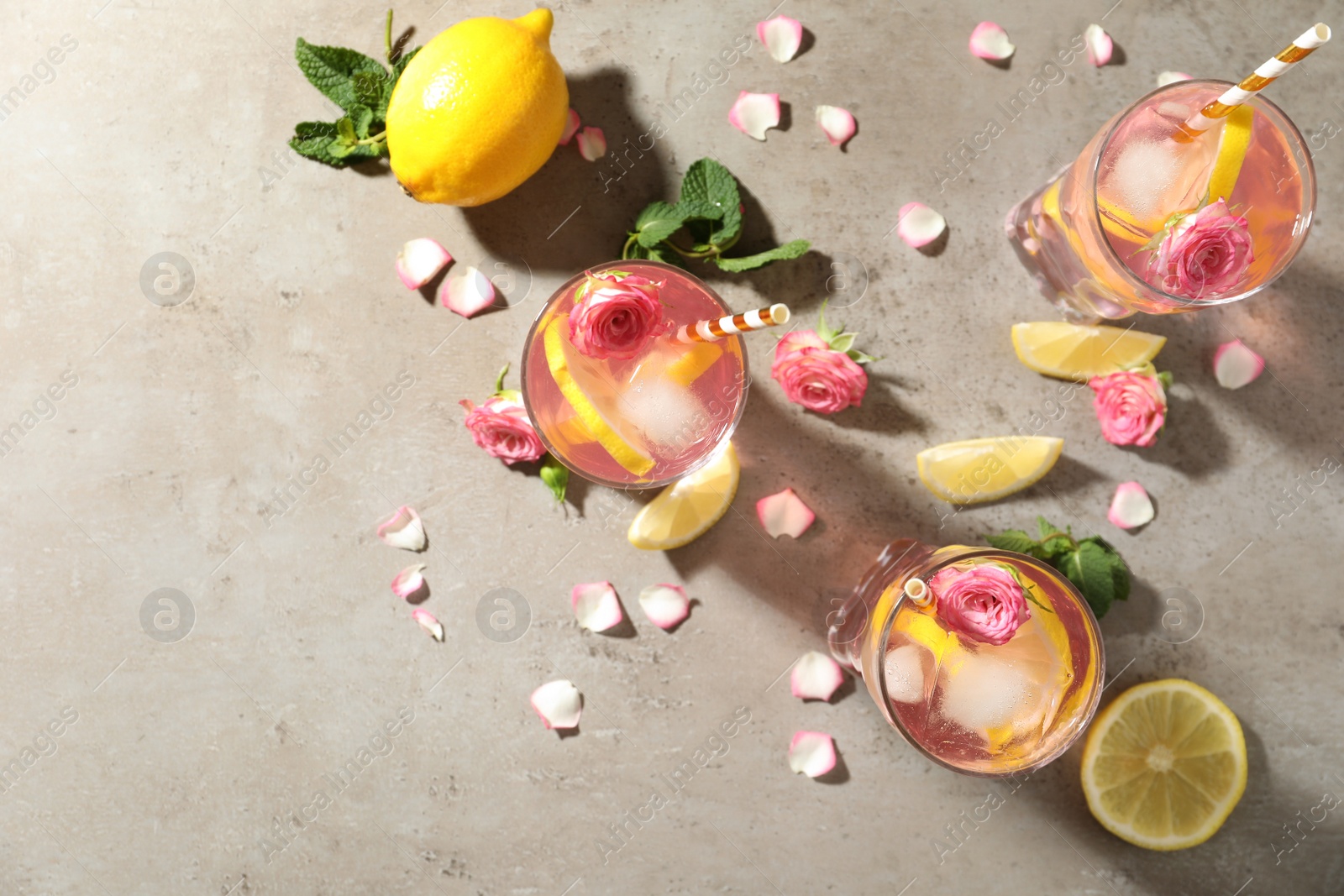 Photo of Delicious refreshing drink with rose flowers and lemon slices on light grey table, flat lay