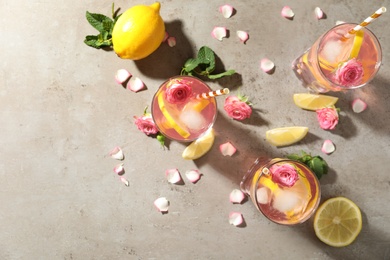 Delicious refreshing drink with rose flowers and lemon slices on light grey table, flat lay
