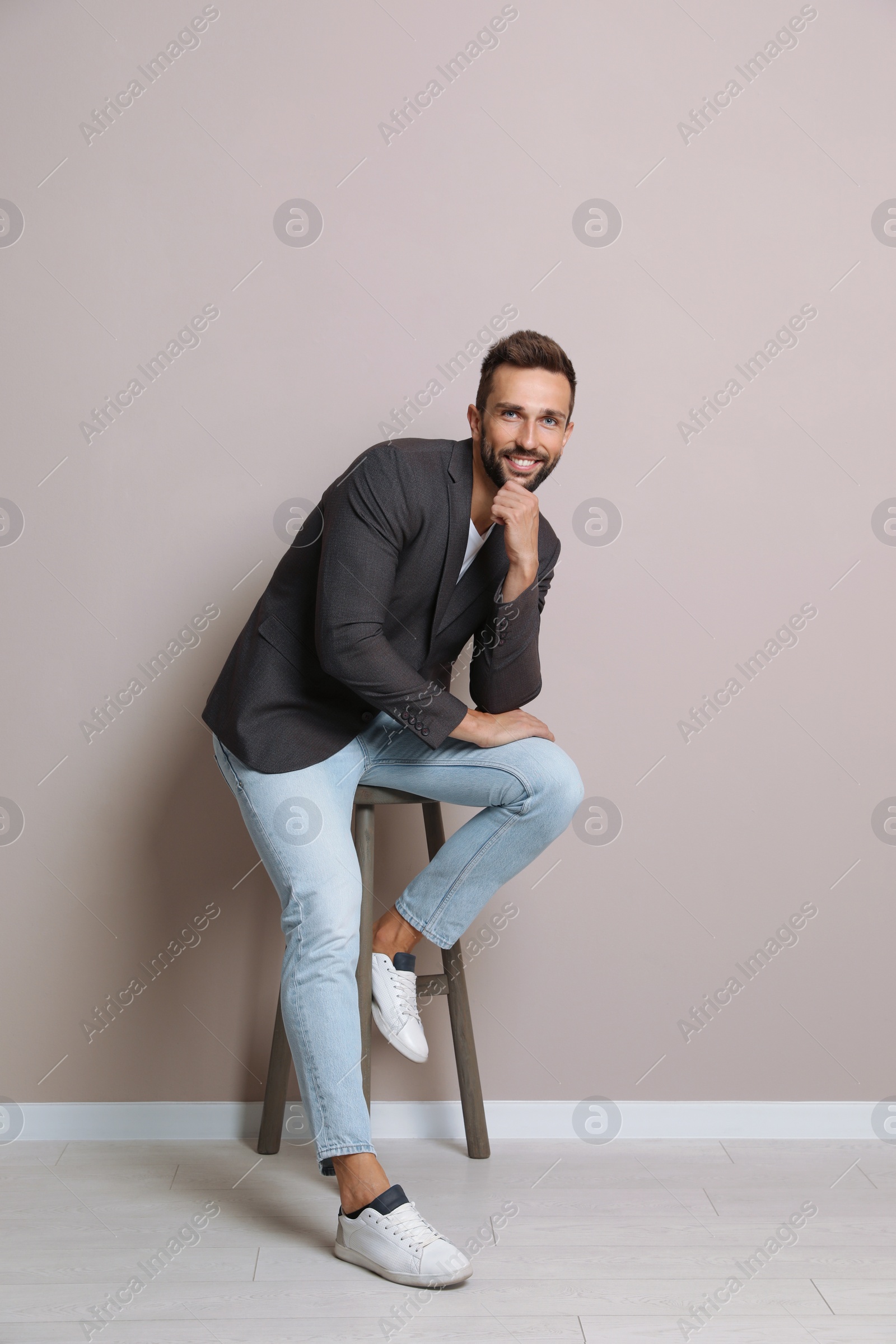 Photo of Handsome man sitting on stool near beige wall