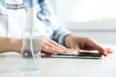 Photo of Woman cleaning mobile phone with cotton pad at white table indoors, focus on antiseptic spray