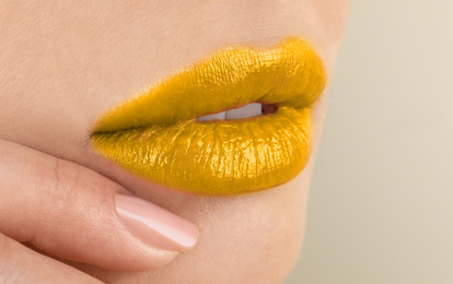 Woman with golden lipstick on beige background, closeup
