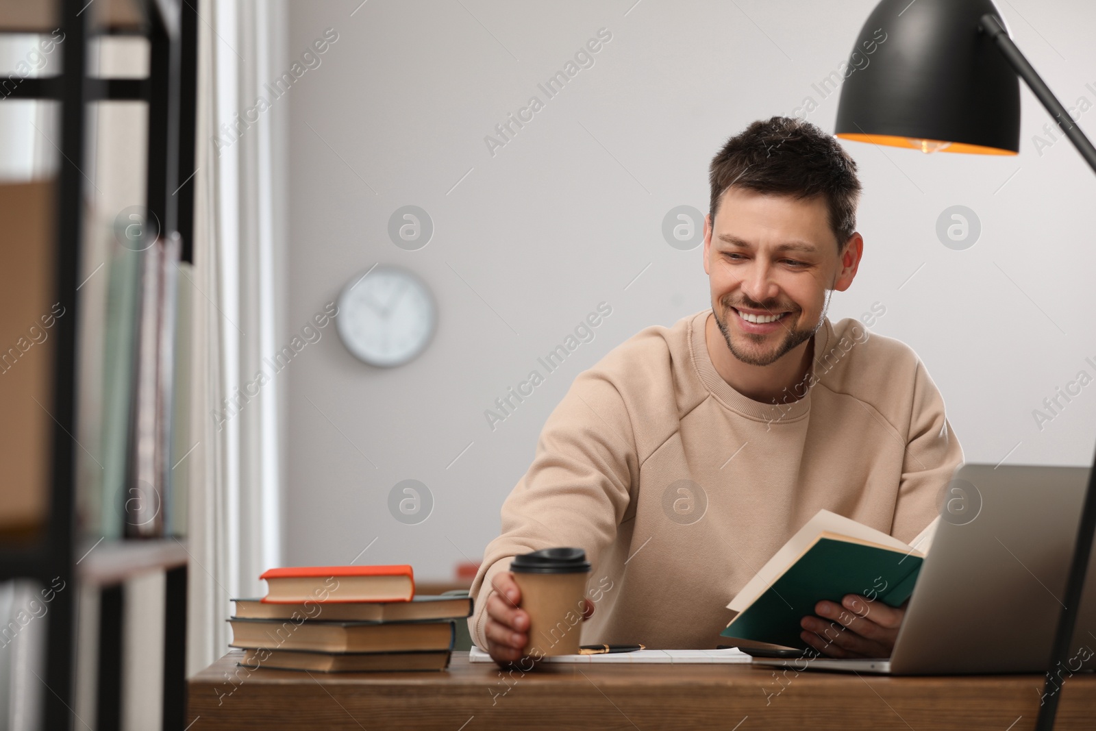 Photo of Happy man with cup of coffee studying in library