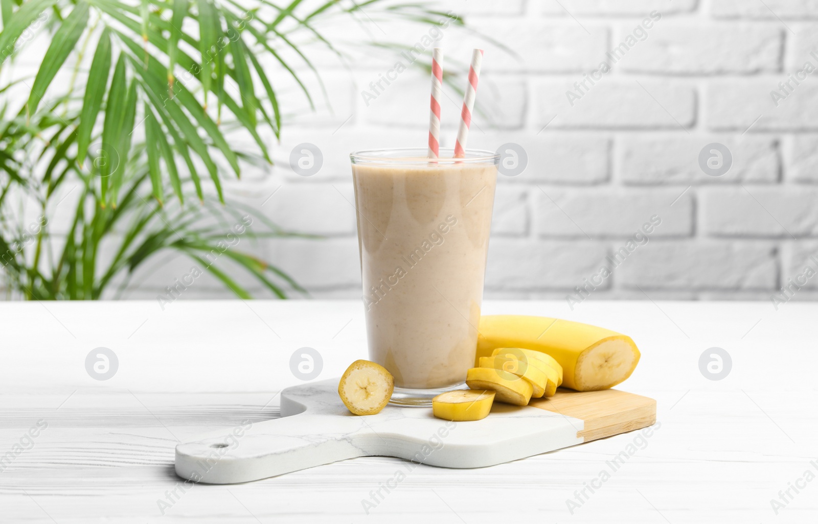Photo of Glass of tasty banana smoothie with straws and fresh fruit on white wooden table