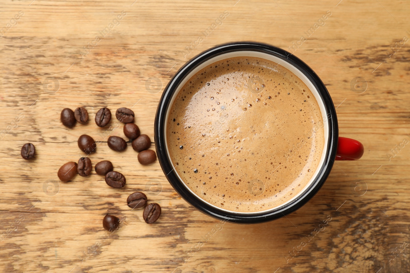 Photo of Cup of aromatic coffee and beans on wooden table, top view