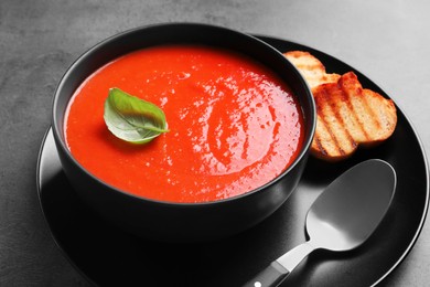 Delicious tomato cream soup in bowl and pieces of grilled bread served on grey table, closeup