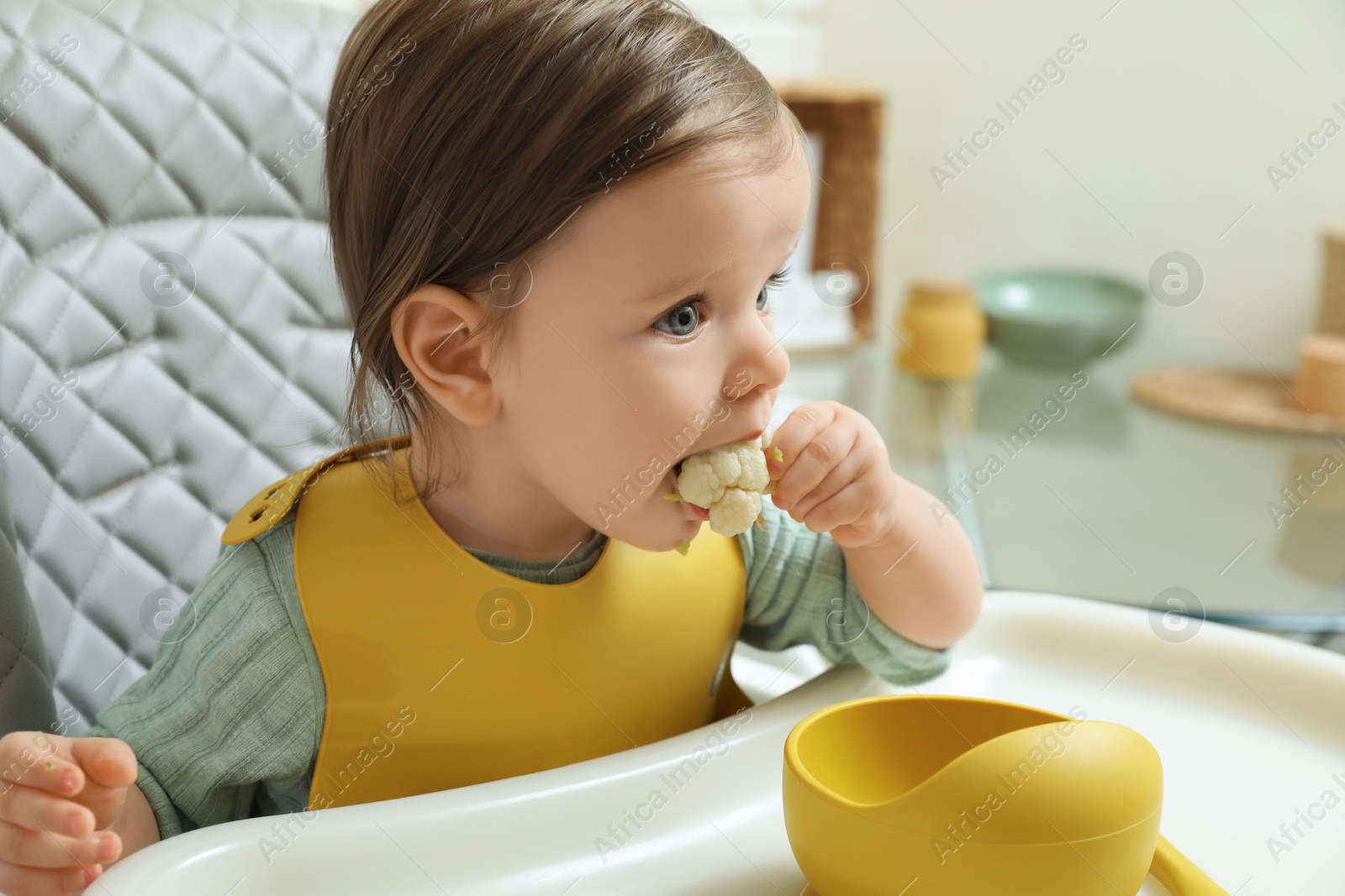 Photo of Cute little baby eating healthy food in high chair indoors