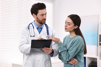 Doctor with clipboard consulting patient during appointment in clinic