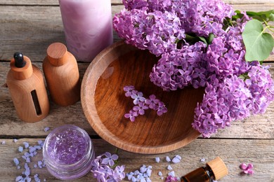 Cosmetic products and lilac flowers on wooden table, above view