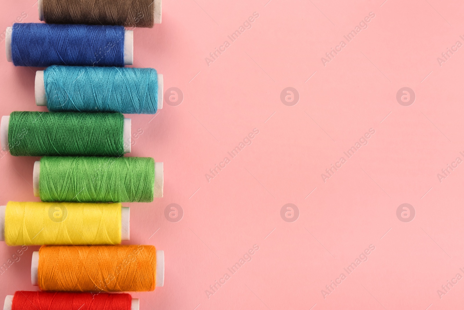 Photo of Different colorful sewing threads on pink background, flat lay. Space for text