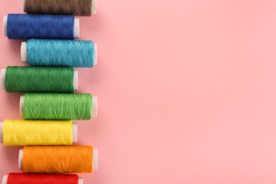 Photo of Different colorful sewing threads on pink background, flat lay. Space for text