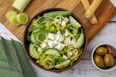 Photo of Bowl of tasty salad with leek and cheese on white wooden table, flat lay
