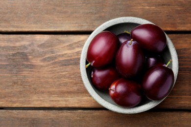 Photo of Tasty ripe plums in bowl on wooden table, top view. Space for text