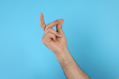 Photo of Man snapping fingers on light blue background, closeup of hand