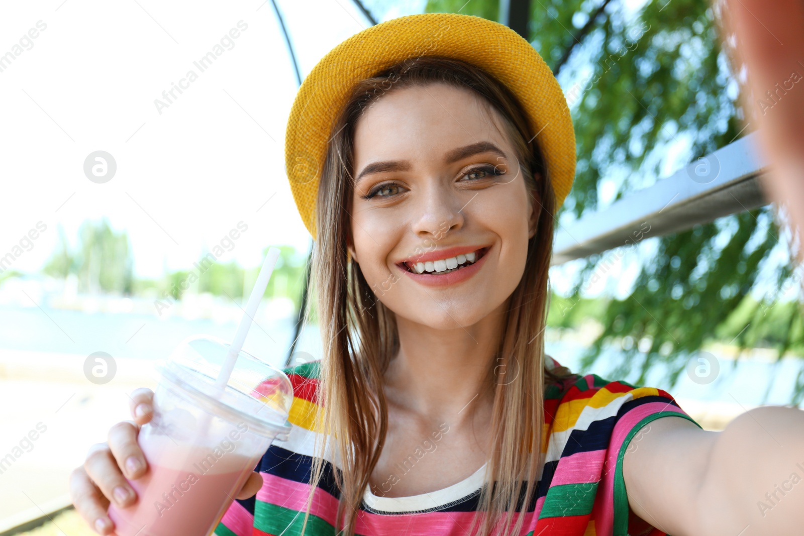 Photo of Happy young woman with drink taking selfie in park