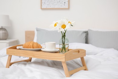 Bouquet of beautiful daisy flowers and breakfast on wooden tray in bedroom