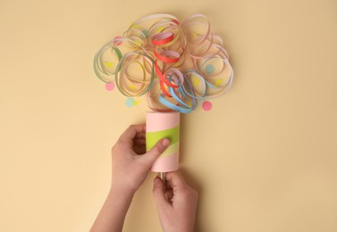 Woman holding party popper with serpentine and confetti on beige background, top view