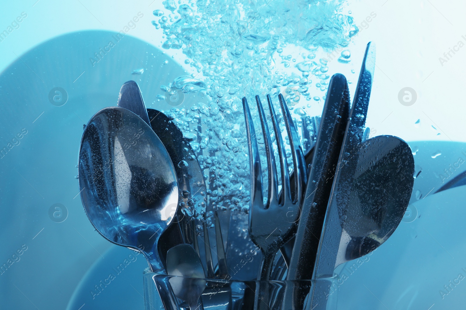 Photo of Washing silver cutlery and plates in water on light blue background