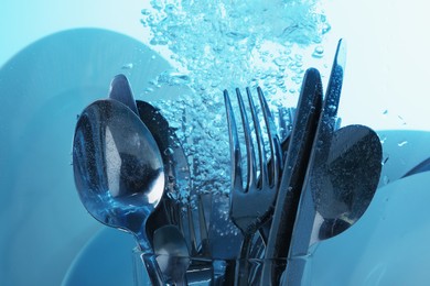 Washing silver cutlery and plates in water on light blue background