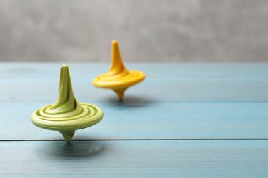 Photo of Bright spinning tops on light blue wooden table, closeup. Space for text