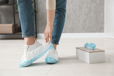 Photo of Woman wearing blue shoe covers onto her sneakers indoors, closeup