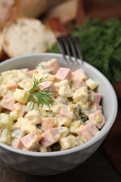 Photo of Tasty Olivier salad with boiled sausage in bowl on table, closeup