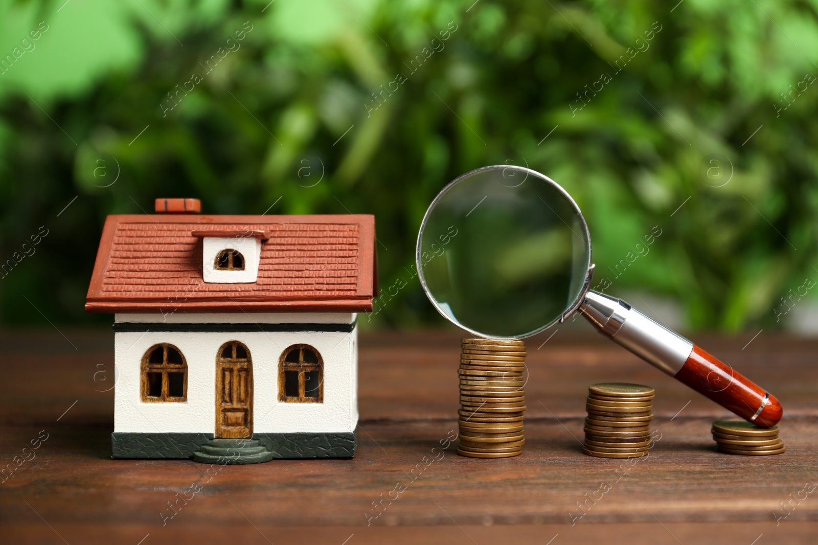 Photo of House model, coins and magnifying glass on wooden table against blurred background. Search concept