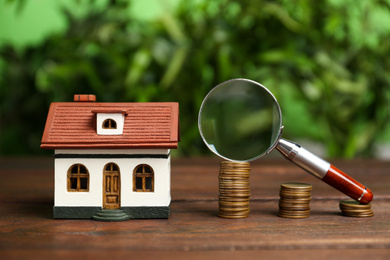Photo of House model, coins and magnifying glass on wooden table against blurred background. Search concept