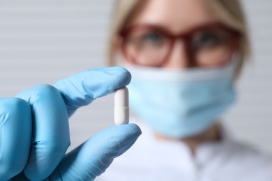 Doctor holding pill on light background, selective focus. Space for text