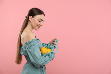 Photo of Woman with string bag of fresh lemons on pink background, space for text