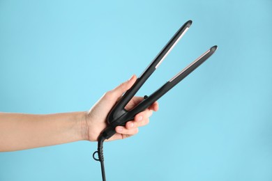 Woman holding flat hair iron on light blue background, closeup