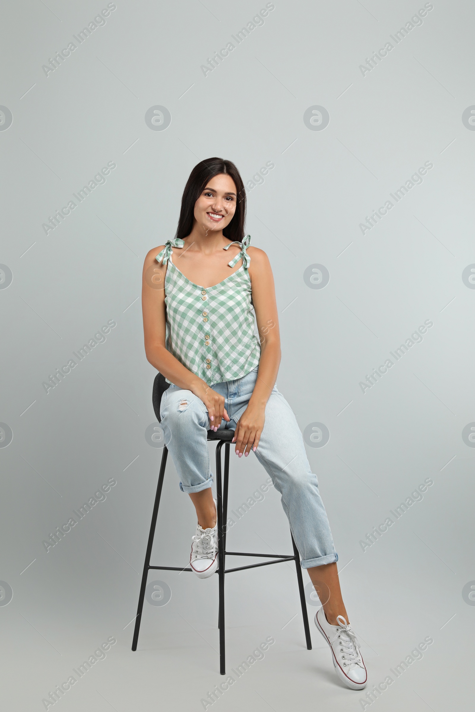 Photo of Beautiful young woman sitting on stool against light grey background