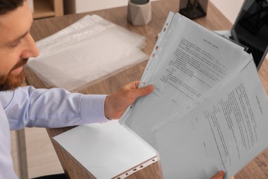 Photo of Businessman working with documents at wooden table in office, closeup