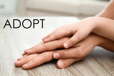 Happy family holding hands at wooden table indoors, closeup. Child adoption concept