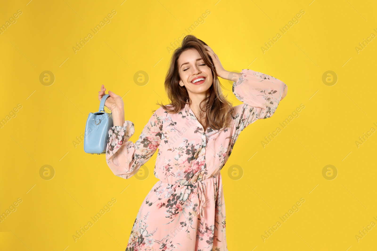 Photo of Young woman wearing floral print dress with stylish handbag on yellow background