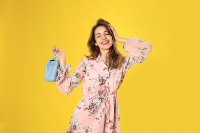 Photo of Young woman wearing floral print dress with stylish handbag on yellow background
