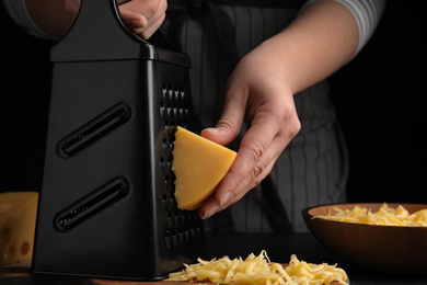 Photo of Woman grating fresh cheese at black table, closeup