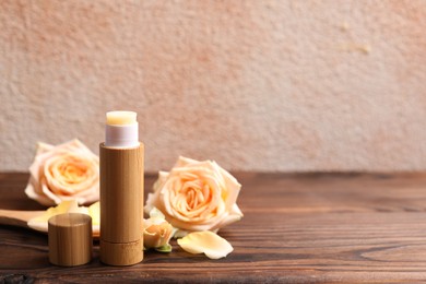 Photo of Lip balm and rose flowers on wooden table, space for text