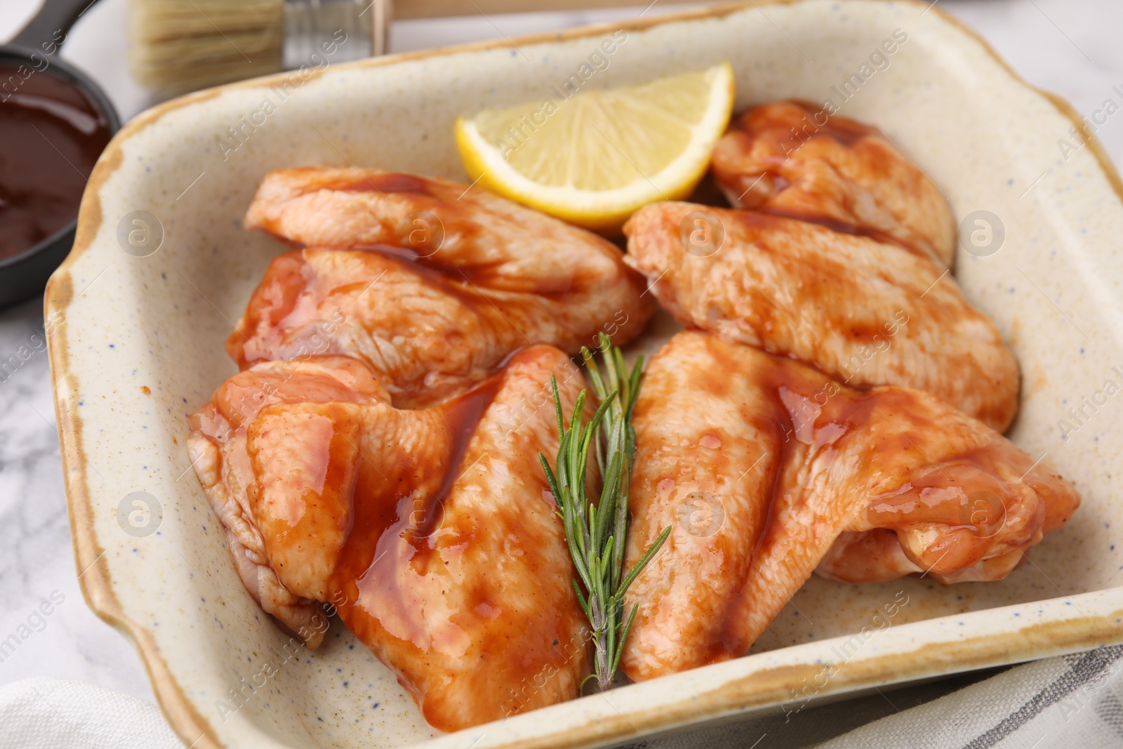 Photo of Raw marinated chicken wings, rosemary and lemon in baking dish on table, closeup