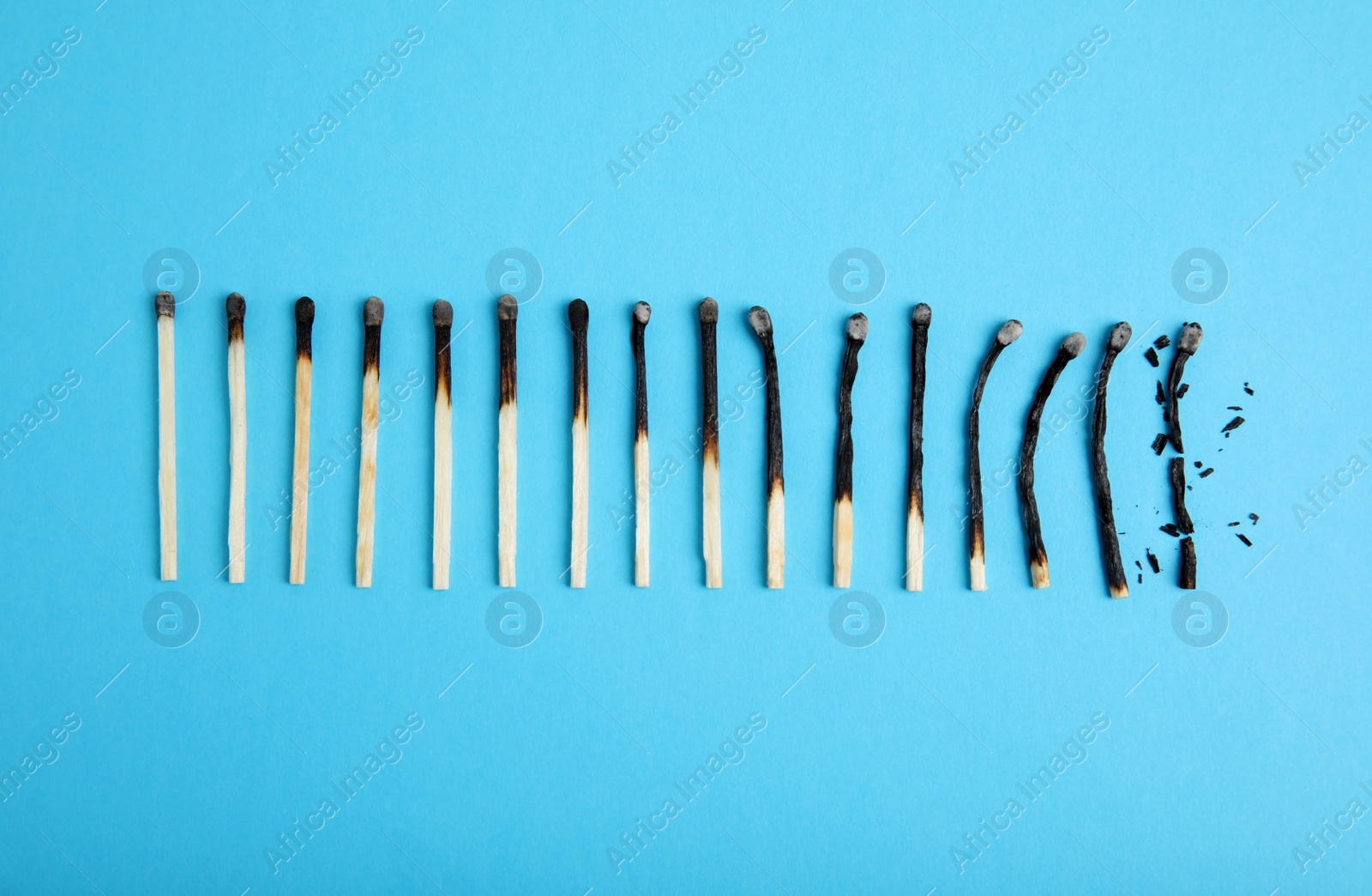 Photo of Different stages of burnt matches on light blue background, flat lay