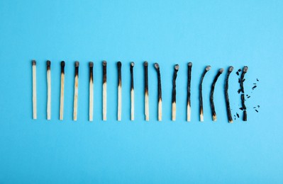 Photo of Different stages of burnt matches on light blue background, flat lay
