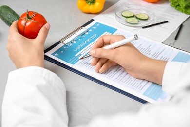 Photo of Scientist with laboratory test form and fresh tomato at table indoors, closeup. Poison detection