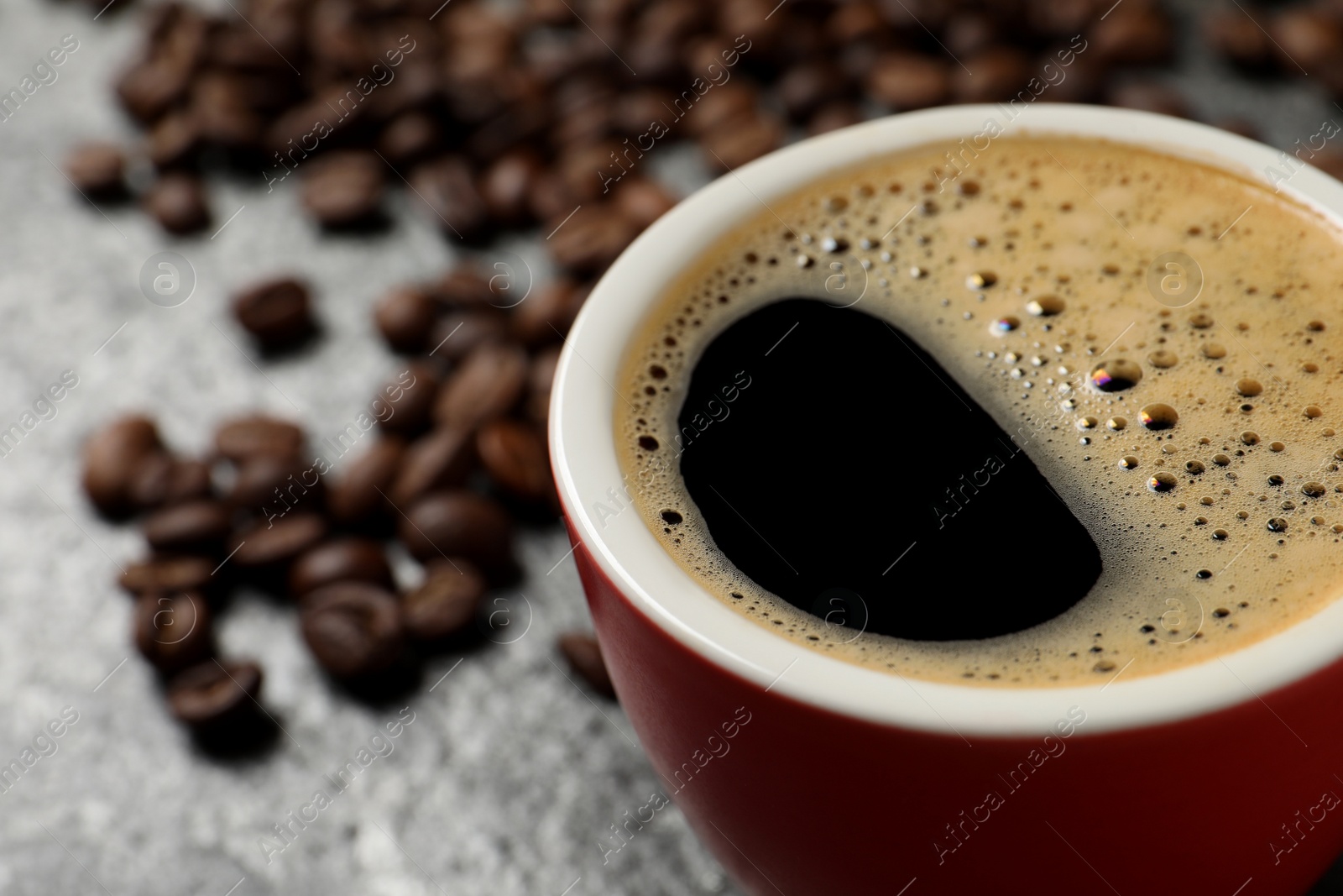 Photo of Cup of aromatic coffee and beans on grey table, closeup. Space for text