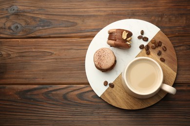 Cup of coffee and delicious macarons on wooden table, top view. Space for text